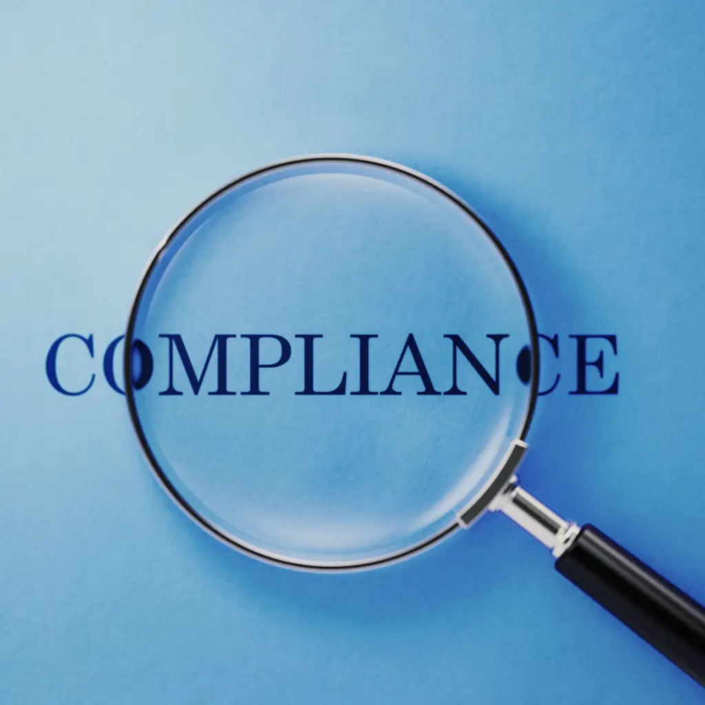The word compliance under a magnifying glass with blue background
