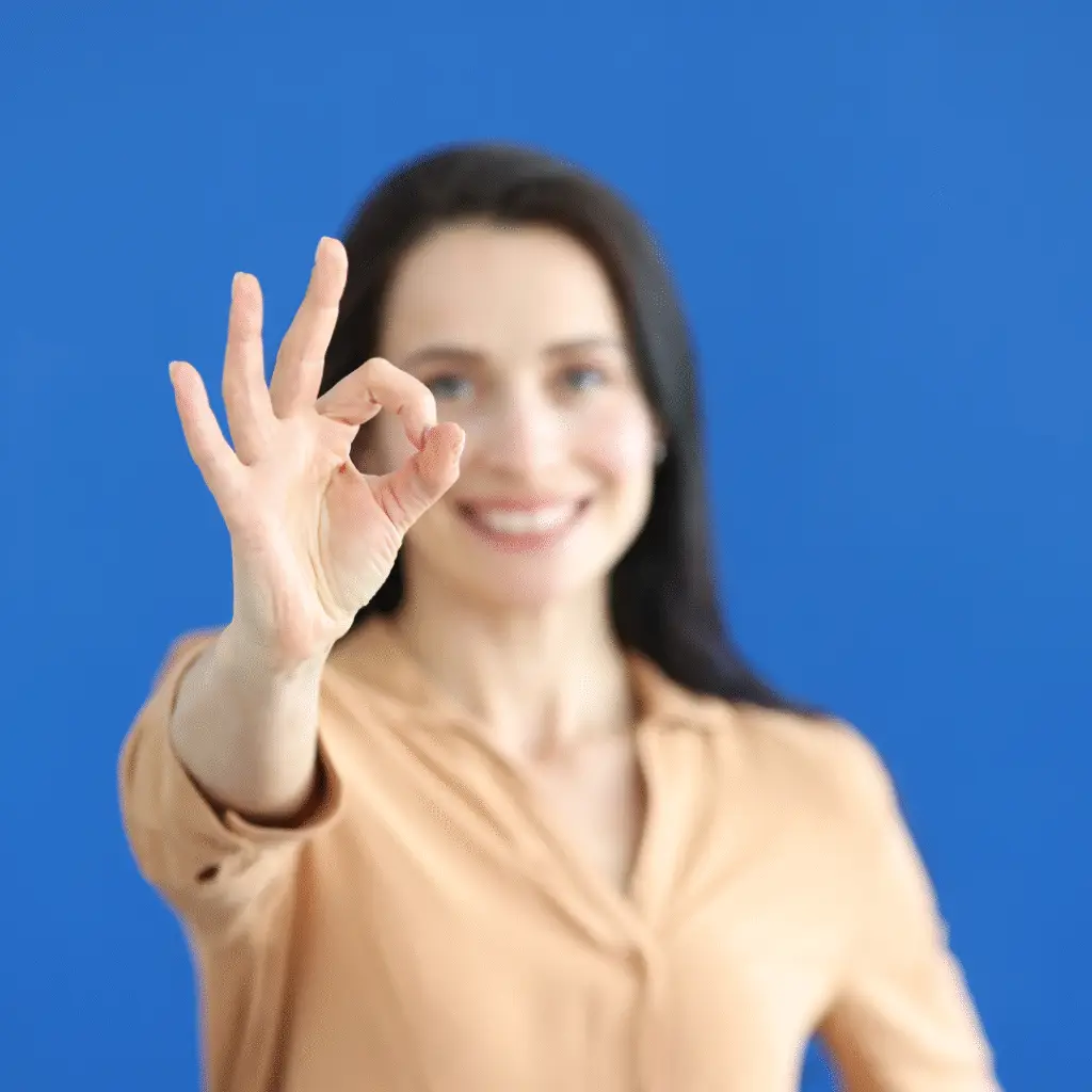 Woman blue background, slightly out of focus, giving the OK sign